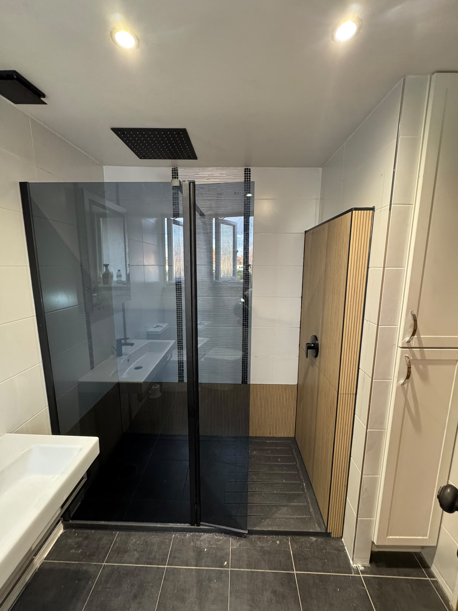 Bath to walk-in shower conversion: black-framed smoked glass screen, ceiling rainfall shower and wood-effect fluted tiles Old bath replaced with a walk-in shower
