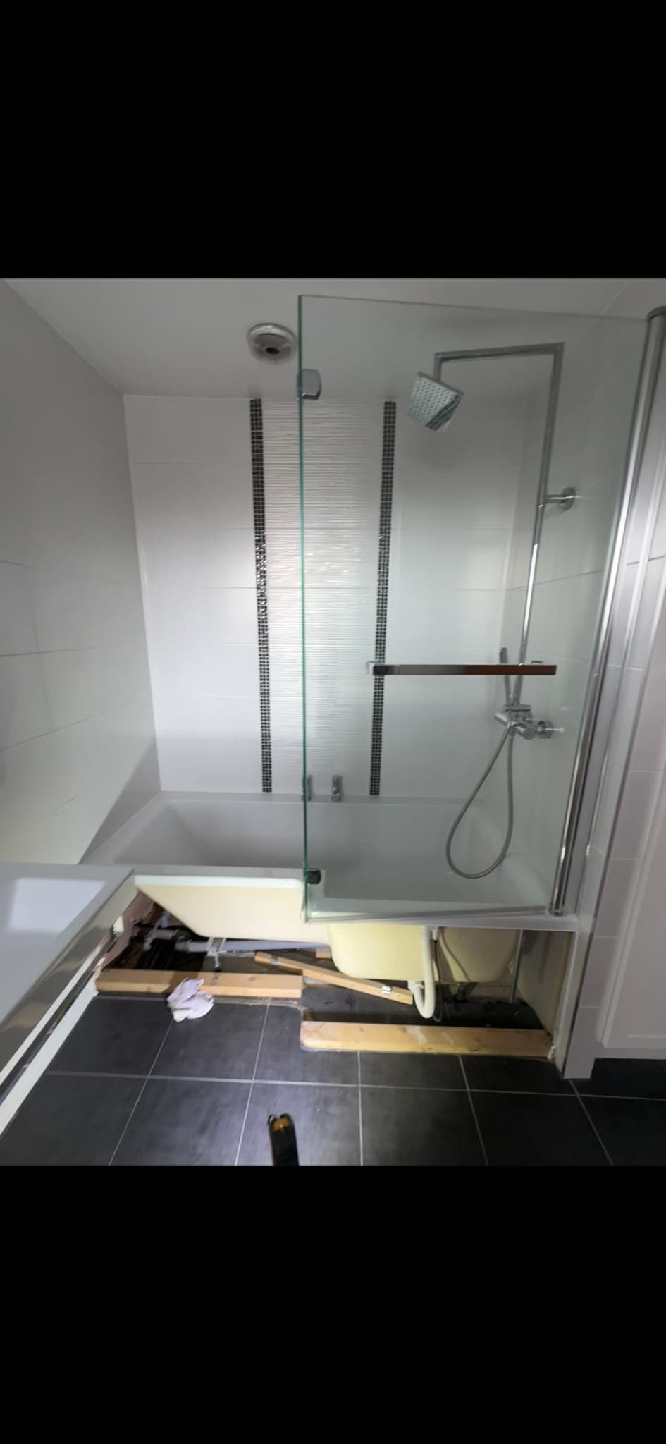 Bath to walk-in shower conversion: black-framed smoked glass screen, ceiling rainfall shower and wood-effect fluted tiles - before