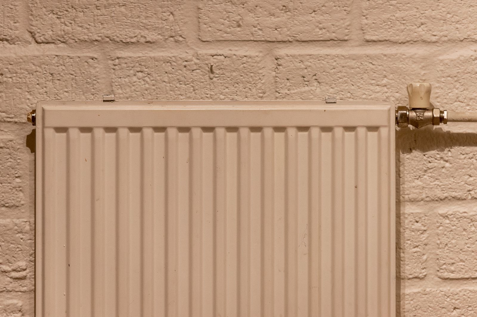 stock photograph of a central heating panel radiator and pipework on a wall. Licensed stock picture, not a photograph of Tami Plumbing, its staff, its premises or a job it carried out.